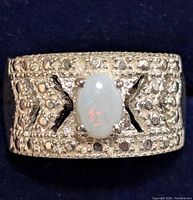 Close-up front view of silver ring with oval opal center stone and detailed textured band with raised dots and cutout design.