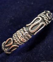 Close-up photo of silver ring showing detailed pattern with twisted rope and elongated loops