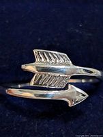 Close-up front view of a sterling silver arrow ring showing detailed fletching and polished finish on a navy background.