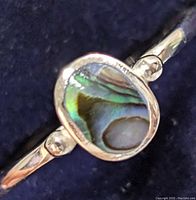 Close-up of the oval abalone shell and silver band showing the ring's colors and details.