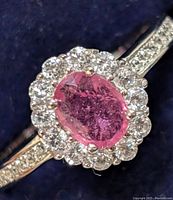 Close-up of the oval ruby center stone surrounded by clear cubic zirconia in a halo setting with additional CZ stones on the band.