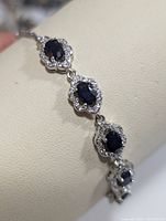 Close-up image showing oval blue sapphires surrounded by clear CZ stones on a sterling silver setting.