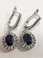 Front view of silver earrings showing oval sapphire center with cubic zirconia surrounding stones and lever-back closure