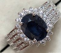 Close-up angled view of the silver ring with dark blue sapphire and surrounding clear CZ stones on triple-row band.