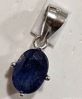 Close-up view of the oval faceted blue sapphire gemstone set in a silver pendant with four prongs and polished silver bail.