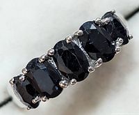 Close-up photo of the front of the silver ring showing the five faceted oval blue sapphires in a prong setting.