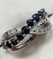 Close-up photo of silver ring showing dark blue sapphire stones set on one band cross and small clear stones on the other crossing band.