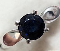 Close-up of silver ring with dark blue sapphire stone, highlighting the rounded, faceted gem and prong setting.