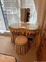 Image showing the fabric covered dressing table with glass top, matching stool, and lighted vanity mirror with bulbs around the frame.