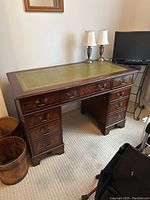 Front view of wooden executive desk with green leather top and twin pedestal drawer bases.