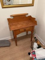 Small pine desk shown against a wall under a mirror, with natural wood grain and turned legs.