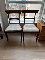 Pair of wooden dining chairs in front of window, showing side-by-side comparison of different backrest styles and similar check fabric seats.