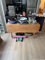 Front view of the pine drop leaf dining table with various kitchen items placed on top including bowls, plates, and glass lantern.