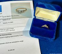 Ring displayed in blue velvet box alongside appraisal document showing image of ring and appraisal text