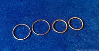 Four yellow gold hoop earrings with different diameters arranged on blue fabric, showing all four hoops together.