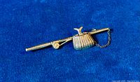 Fishing rod brooch laid flat against blue fabric, showing the detailed rod, reel, creel basket with a fish figure and attached chain.