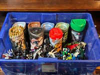 Top view of blue plastic bin containing multiple LEGO Bionicle cylindrical containers and loose parts inside the bin.