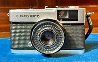 Front view of Olympus Trip 35 camera showing silver body with black textured grip and lens details.