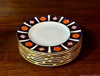 Stack of eight Royal Crown Derby 'Old Imari' bread plates showing decorative borders and gilded edges.