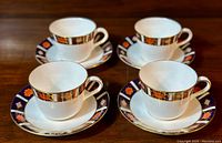 Set of four Royal Crown Derby Old Imari teacups with matching saucers arranged on a wooden surface.