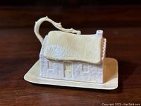 Front and side view of the cottage butter dish showing the thatched roof style lid, textured walls with door and windows, and flat base plate.