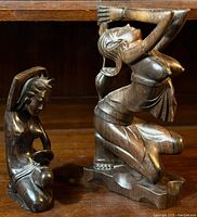 Two carved teak wood sculptures of women posing, shown side by side for scale.