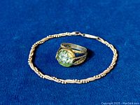 Both the sterling silver ring with raw greenish-yellow gemstone and the sterling silver rope weave bracelet on blue fabric background.