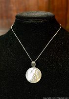 Front view of necklace displayed on black velvet bust showing round iridescent mother of pearl pendant on sterling silver chain.