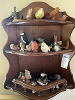 Full view of wooden wall-mounted display shelf holding multiple bird figurines on three shelves.