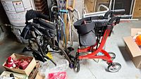 Photo showing black foldable wheelchair, multiple walking sticks, and red walker grouped together in basement setting