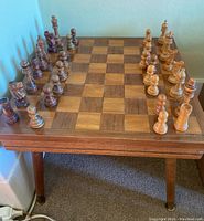 Wide angle photo showing the wooden chess and checkers table with inlaid board and wooden chess pieces set in starting position.