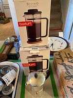 Two boxed Bodum Bistro French presses stacked on top of each other with a classic aluminum Moka pot in front on a table surface.