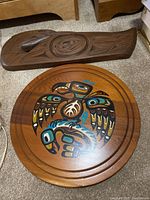 Photo showing the carved wood art piece and round painted Thunderbird plaque on carpet.