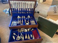 Open wooden flatware chest showing upper knife rack with 12 dinner knives and lower tray with forks and spoons