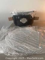 Harley Davidson branded black charcoal BBQ grill with logo visible, wrapped components including grill grate and metal legs laid out separately