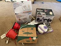 Photo showing boxed Vtech amplified cordless answering system, boxed Goldbeam Producer II film-to-video transfer system, two red lamps with cords, and two hummingbird feeders in boxes plus a spool.