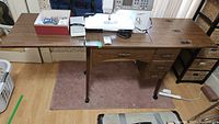 Full view of sewing machine setup on wooden cabinet with drawers, accessories and foot pedal visible