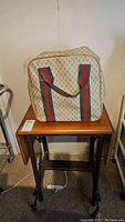 Protective fabric cover for the Elna Lock serger sewing machine with distinctive green and red stripes on the handles sitting on the wooden table.