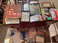 Wide view of table with stamp albums, loose stamps in packages and pages spread out.
