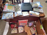 Table with two stamp albums, ziploc bags with loose stamps, first day cover album and multiple loose envelopes and packets of stamps and covers.