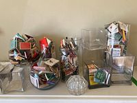 Photo showing the assortment of eight glass vases filled with a vintage matchbook collection, plus a small glass flower frog in front.