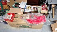 Wide view showing several boxes of vintage glass Christmas ornaments, some unpacked ornaments, holiday linens, and boxed fiber optic tree components.