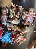 Full view of the collection of vintage dolls arranged on the floor including dressed and undressed dolls, and boxed accessories.