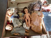 Overview of vintage dolls and accessories inside a vintage suitcase including multiple dolls and doll heads, clothing.