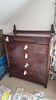Front view of tall vintage wooden dresser showing five drawers with brass handles and lock tags attached.