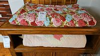 Two folded quilts on a wooden table, one floral pattern on top and one pale with tulip appliques underneath.