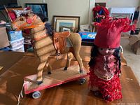 Photo showing the horse pull toy on wooden wheeled base and the ethnic doll side by side on table