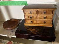 Photo showing carved wooden bowl, small multi-drawer jewelry box, and lacquered decorative box on shelf.