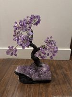 Front view of 15 inch amethyst gemstone tree with polished amethyst leaves on raw amethyst base on wooden floor.