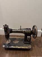 Front side view of the black White Rotary sewing machine with gold decorations on a wood floor against a white wall.